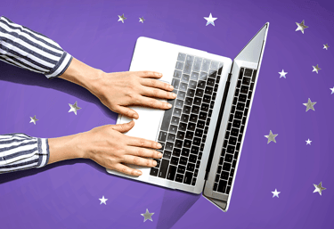 Hands typing on a laptop that is sitting on a purple surface covered in silver stars.