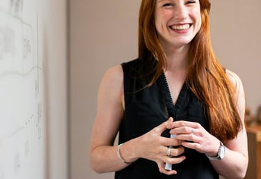 A smiling woman holds a marker and stands next to a white board in the front of a board room.