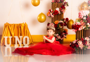 a baby girl in a red dress sitting on a floor