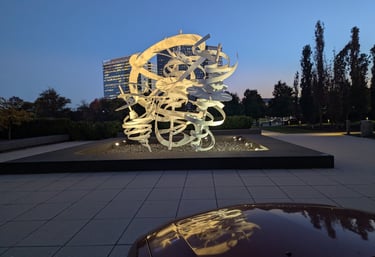 a sculpture and modern buildings during the golden hour