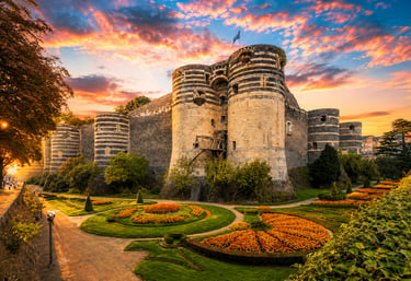 The historic Chateau d'Angers castle in France featuring striped towers and formal gardens at sunset.