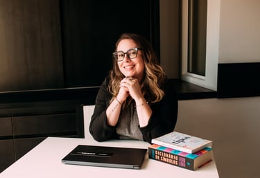 Foto da Ro Lammers sorrindo em sua mesa de trabalho, com notebook e livros.