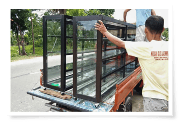 A worker loads several aluminum window frames onto a pickup truck in a sunny outdoor setting.