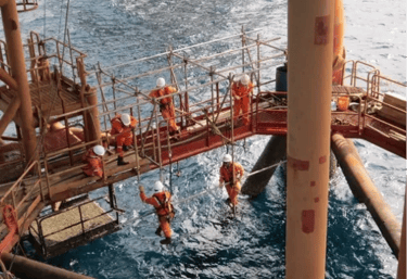 Offshore oil rig workers performing maintenance on scaffolding over the ocean.