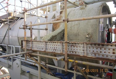 Industrial boiler with damaged thermal insulation and scaffolding at an oil and gas facility.