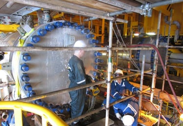 Industrial technicians performing maintenance on a large heat exchanger at an offshore oil rig.