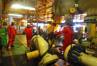 Offshore oil rig engineers in orange coveralls performing heavy lifting and pipeline maintenance.