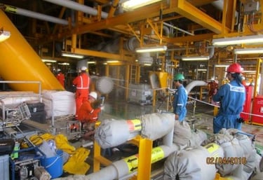Industrial offshore oil rig workers wearing safety gear performing maintenance on yellow steel pipes.