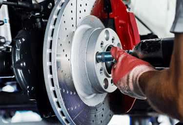 person with red gloves holding a car tool fixing a brake.