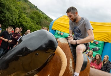 A man riding a rodeo bull at Cwmdu and District Show infront of a crowd