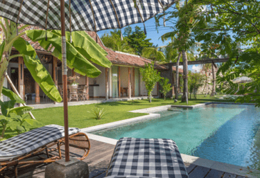 Shimmering swimming pool surrounded by tropical plants, sun loungers, and joglo with modern amenity