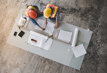 two men in safety vests and hard hats working on a table