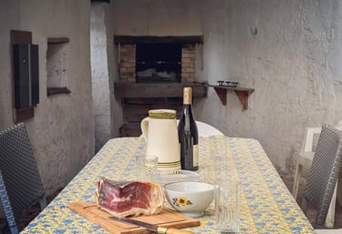 Une table sur la terrasse avec un morceau de jambon, une carafe et une bouteille de vin posée dessus