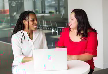 two women sitting at a table with a laptop