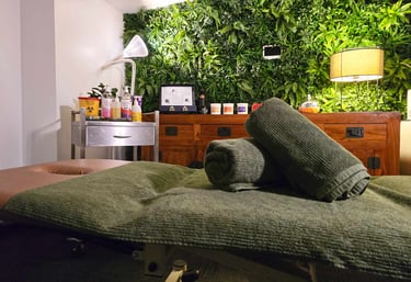 calm tranquil photo of a massage studio with the massage bed at the front and green wall in the back