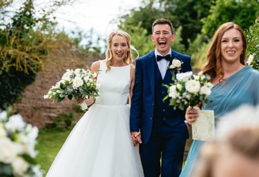 Bride and groom laugh as they walk hand in hand at a South Wales countryside wedding, captured by photographer Owen Mathias