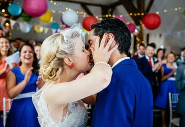 a bride in vintage dress and groom in blue suit kissing at a wedding ceremony