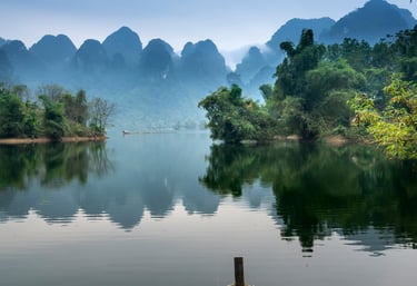 Ein asiatisches kleines Boot an einem Ufer mit schau auf einen Fluss und Hügel im Hintergrund.