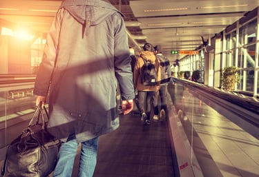 A line of travellers carrying bags queues at an airport check-in