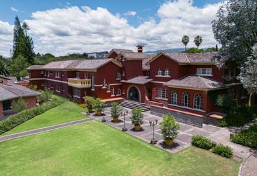 Fotografía aérea de gran casa religiosa de color rojo rodeada de hermoso jardín verde en Quito Ecuador