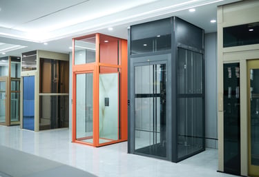 Modern glass home elevator models in a showroom featuring orange and black frames for residential accessibility.