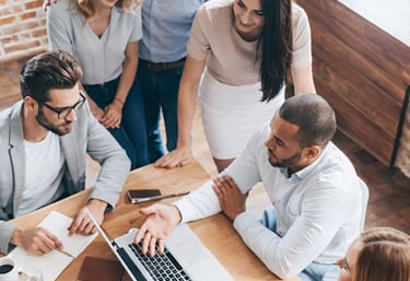 Diverse creative business team collaborating on a laptop project during a strategy meeting in a modern office.