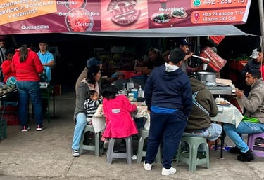 Puesto de Carnitas y Barbacoa NITO con clientes comiendo en mesas bajo una lona en un mercado