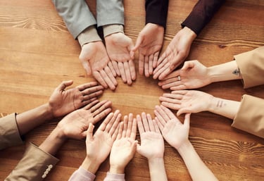 Meerdere handen vormen een cirkel met handpalmen omhoog, beeld van contact en luisteren.