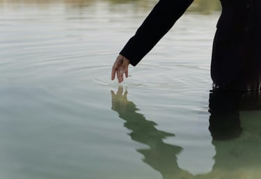 “Silhouet van persoon staand in water, hand raakt oppervlak, symboliseert introspectie.