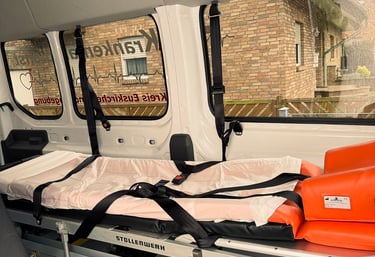 Innenraum eines Krankenfahrdienstes mit leerer Trage neben Fenster Backsteingebäude außen sichtbar.