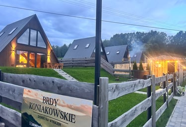 Modern A-frame wooden cabins at Brdy Koniakowskie resort with evening lighting and mountain views.