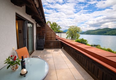 Luxury lakefront balcony with a glass table and wine overlooking scenic mountains and blue water.