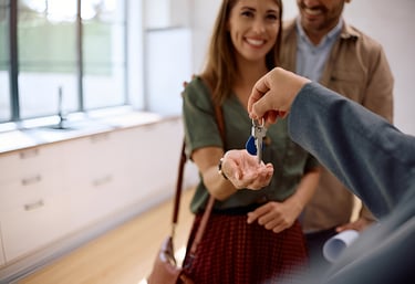 Mujer recibiendo llave de su nueva vivienda en compañía de su pareja, reflejando entrega de proyecto