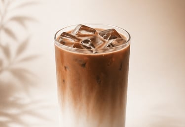 Iced coffee latte with milk and ice cubes in a glass on a beige background with leaf shadows.