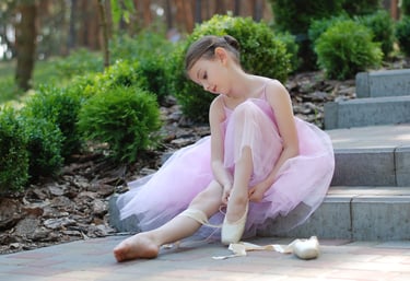 A young girl in a ballerina tutu fixes her ballet slipper.