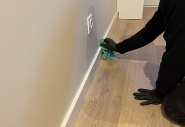 Nettoyage plinthes avec gants noir et chiffon vert sur parquet couleur bois