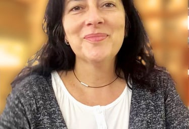 Smiling woman with long dark hair wearing a grey cardigan and white blouse in a professional setting.