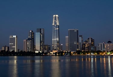A sharp, clear image of a modern city skyline in Faridabad at night, with illuminated buildings reflecting in a still body of water. The mood is sophisticated and prosperous, utilizing the brand's dark and muted blue tones.