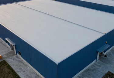 Wide aerial shot of a finished industrial project in North America. A vast warehouse roof with clean architectural lines, finished in Light Gray and Dark Blue tones. The professional setting reflects durability and authority.