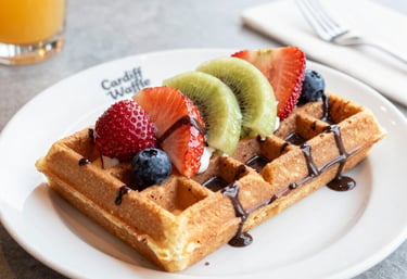 A close-up of a golden waffle topped with fresh strawberries and drizzled with rich Belgian chocolate sauce.