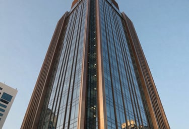 A sophisticated and prestigious brand identity conveying architectural excellence, trust, and luxury living. Low-angle photography of a contemporary commercial office tower with metallic bronze fins and reflective glass panels in a Middle Eastern / Gulf business district under clear blue sky.