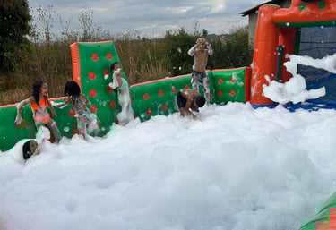 Excited children playing in a large inflatable foam pit at an outdoor summer party.