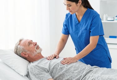 A male nurse in blue scrubs provides bedside care to an elderly patient in a hospital bed.