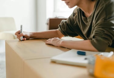 A person using a permanent marker to label a cardboard moving box for organization during a home relocation.
