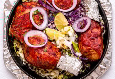 Tandoori chicken drumsticks served in a cast iron skillet with red onions, cabbage, and lime wedges.