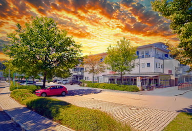 Modern white hotel building and parking lot under a vibrant orange sunset sky.