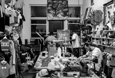 Fotografía en blanco y negro de un taller de confección muy concurrido, con ropa para mascotas.