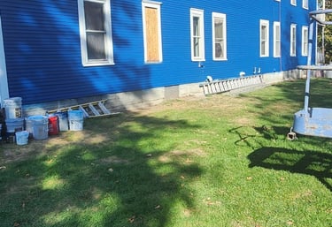 A vibrant blue house with white trim, surrounded by painting supplies, suggests a recent or ongoing exterior home renovation