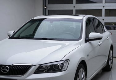 A shiny, perfectly repaired sedan parked in a modern North American garage. The front windshield is crystal clear, catching the light. Professional and high-quality craftsmanship.