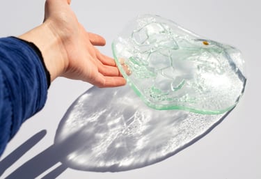 Una mano extendiéndose hacia un cuenco texturizado de vidrio, proyectando reflejos de luz brillante